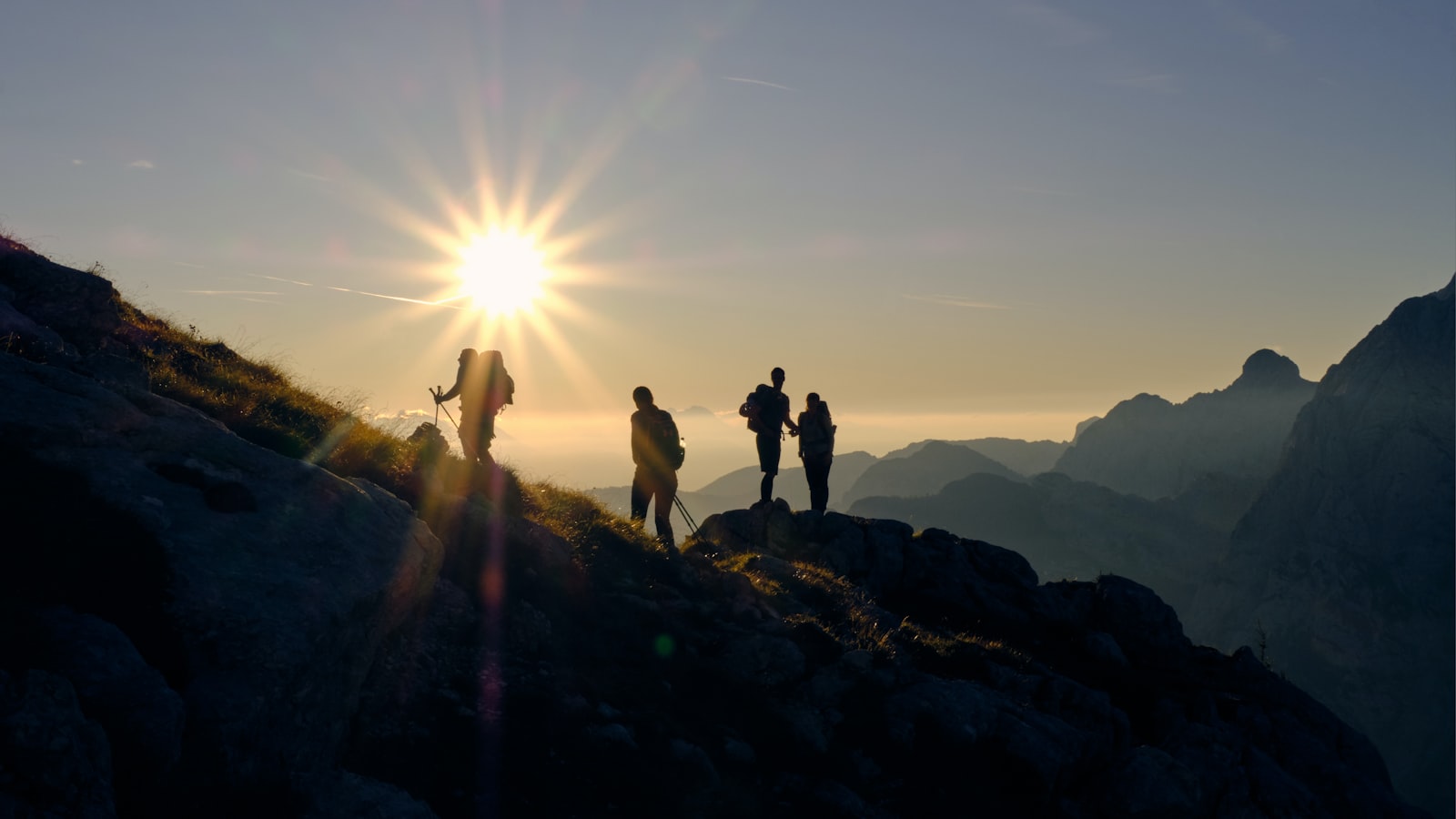 Four hikers silhouetted on a mountain ridge at sunrise